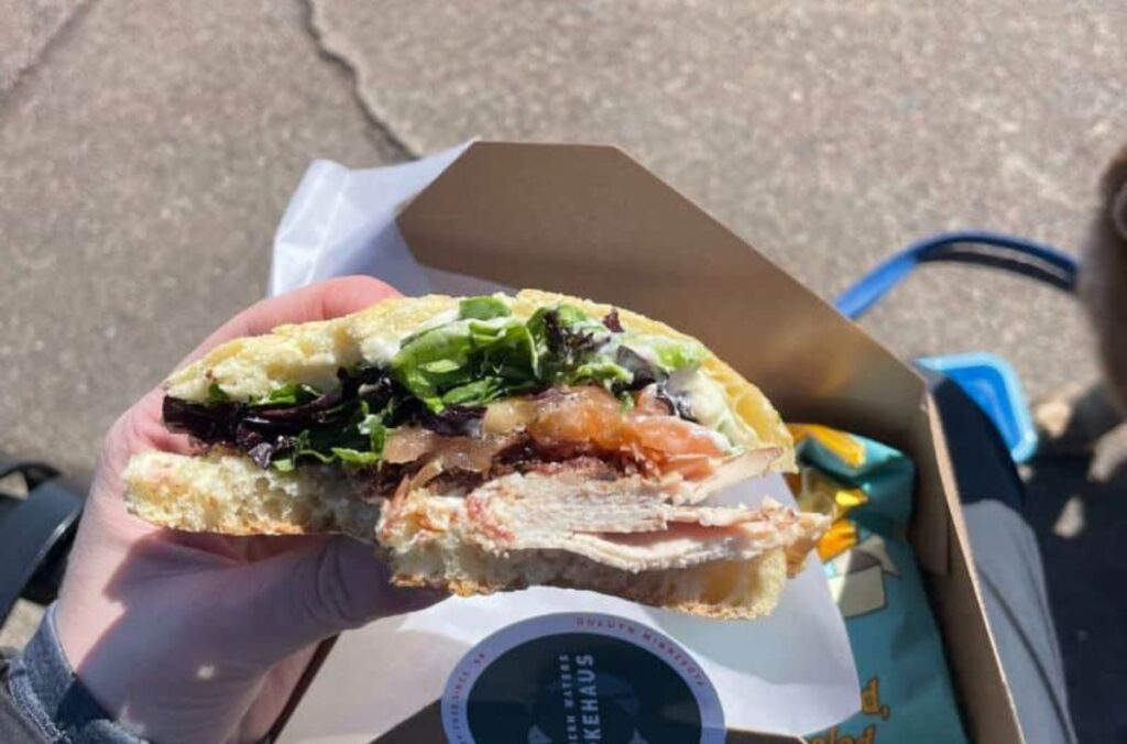 A person holding a sandwich that has lettuce, tomato, and deli meats on it with a few bites taken out of it.