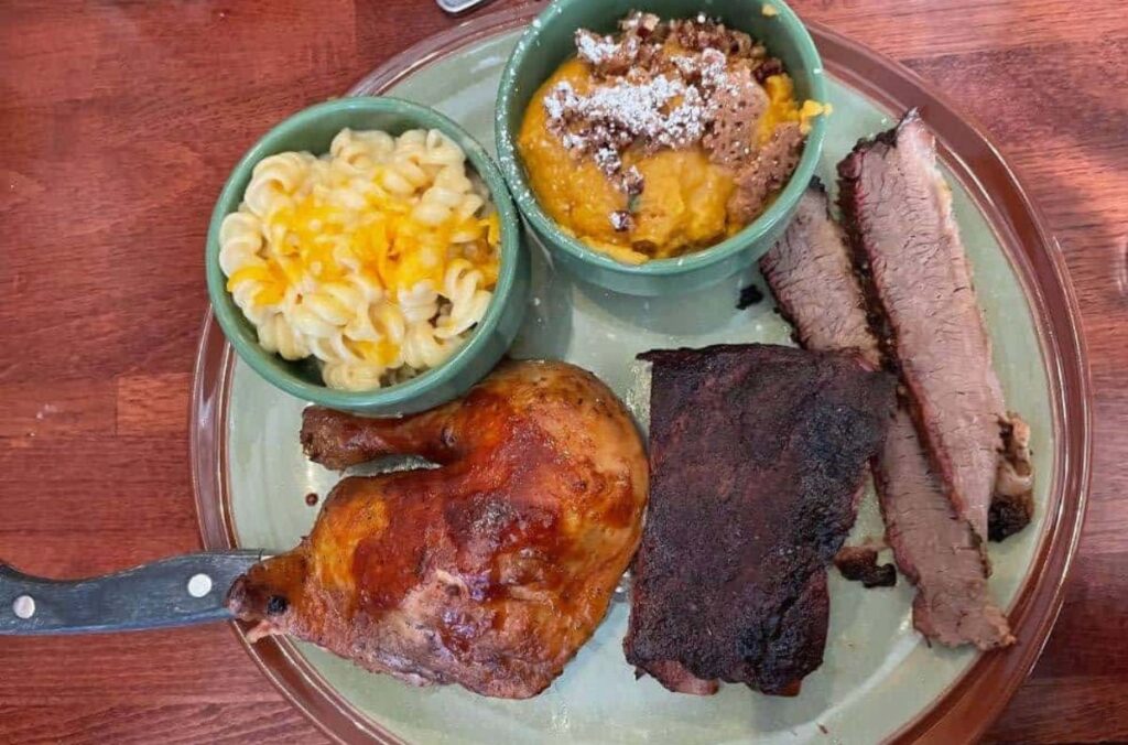 A green plate with barbeque meats, mac and cheese, and sweet potato casserole.